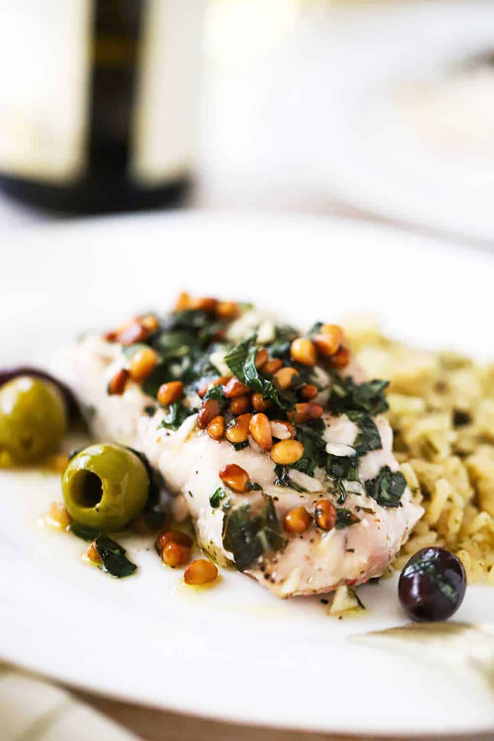 A white plate holding a serving of Mediterranean-style baked red snapper with a side of cooked wild rice. 