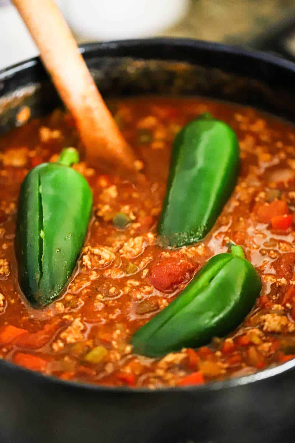 A pot filled with turkey chili with three fresh jalapenos floating on top.