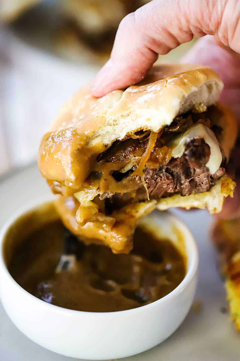 A hand holding a leftover pot roast slider with a bite taken out of it after being dipped in brown gravy. 
