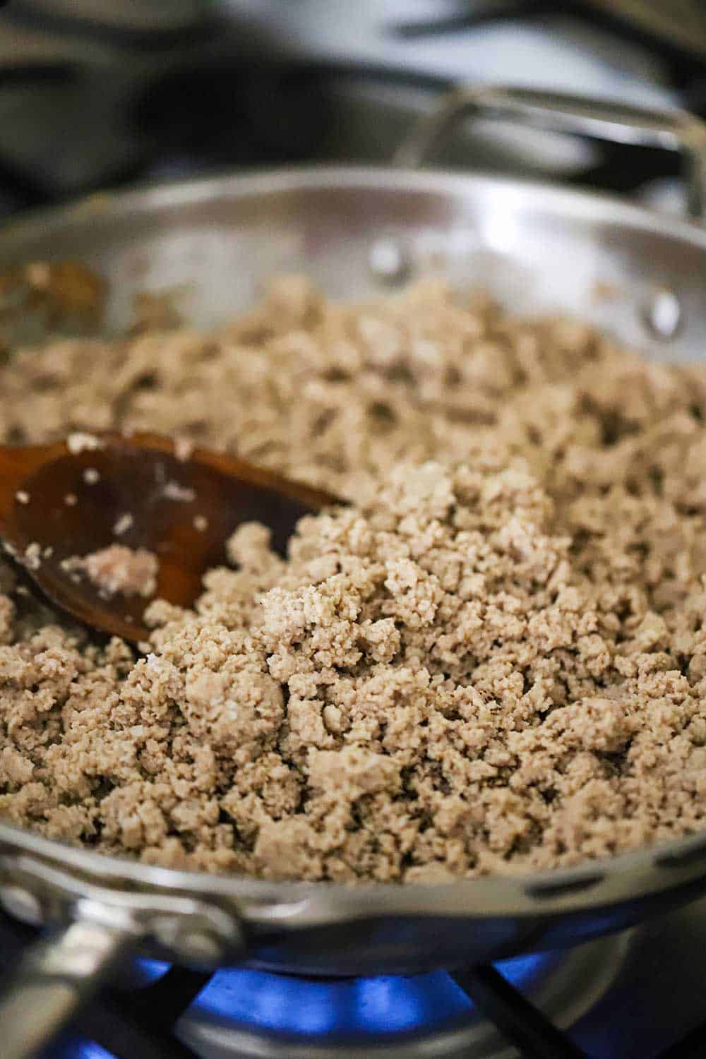 A large stainless steel skillet filled with fully cooked ground turkey.