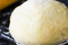 A ball of pizza dough sitting on a floured black surface next to a rolling pin.