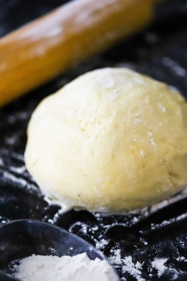 A ball of pizza dough sitting on a floured black surface next to a rolling pin.
