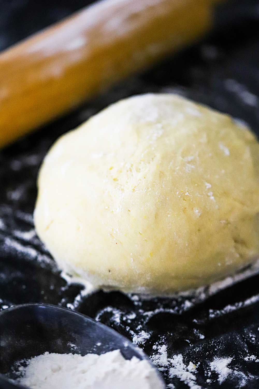 A ball of pizza dough sitting on a floured black surface next to a rolling pin. 