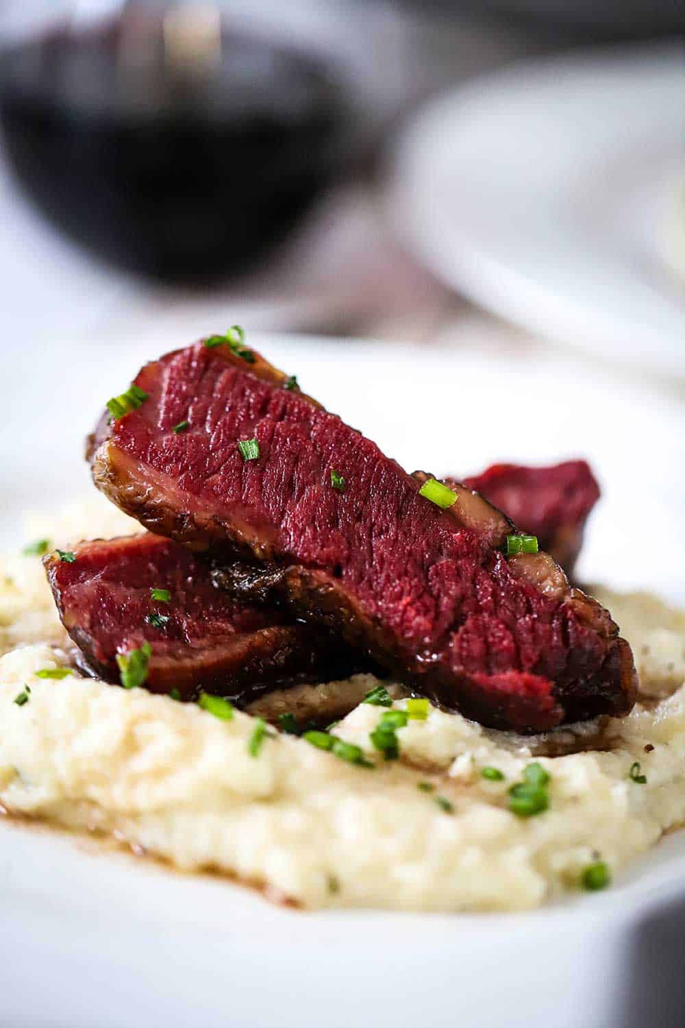 Two slices of Wagyu chuck short ribs that are stacked on top of mashed cauliflower all on a white dinner plate. 