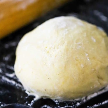 A ball of pizza dough sitting on a floured black surface next to a rolling pin.