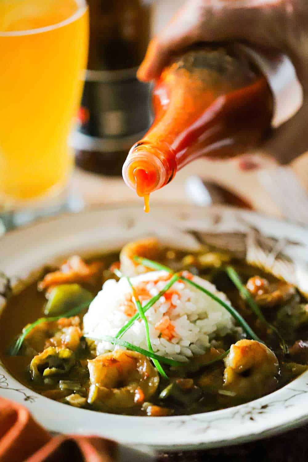 A bottle of Crystals hot sauce is being poured onto a bowl filled with shrimp gumbo with a mound of white rice in the middle. 