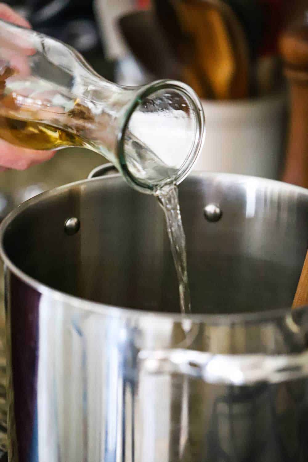 White wine being poured from a carafe into a large silver stock pan.