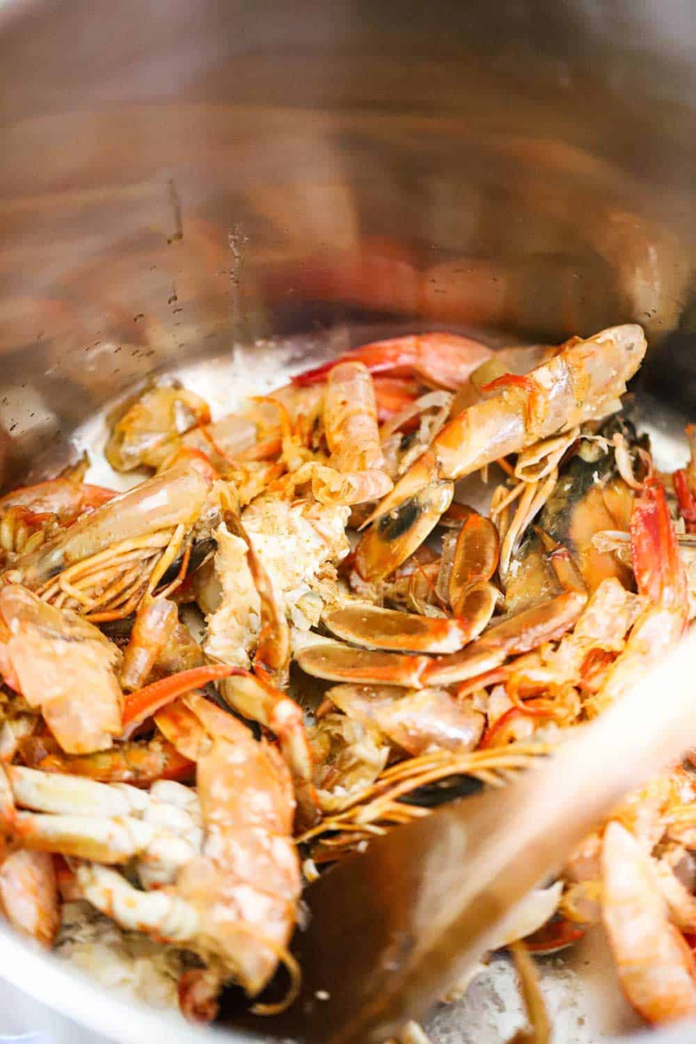 Shellfish shells being sautéed in a large stock pan with a wooden spoon in it.