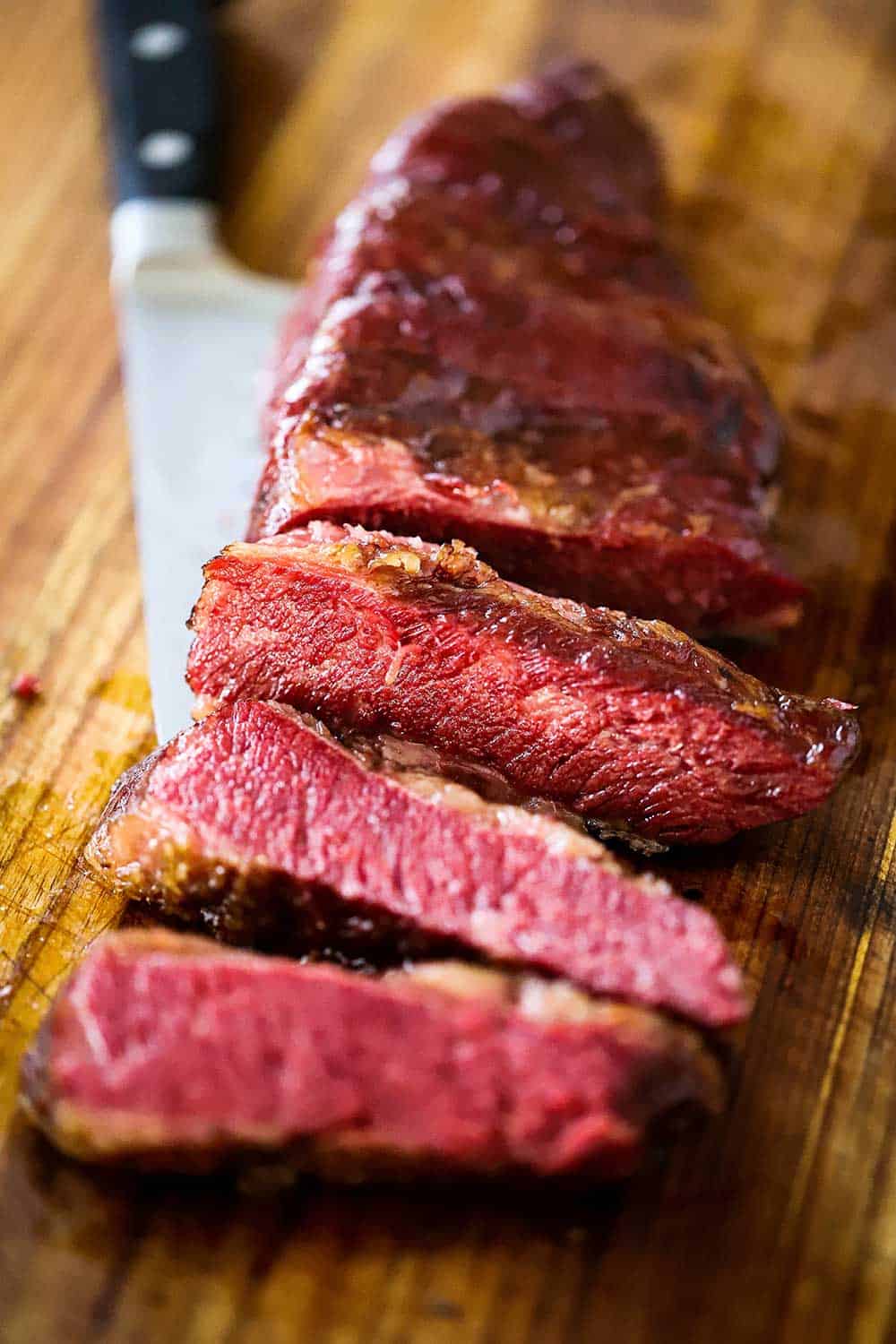 A cut of Wagyu chuck short ribs on a cutting board that has been cut into slices all sitting on top of the chef's knife. 