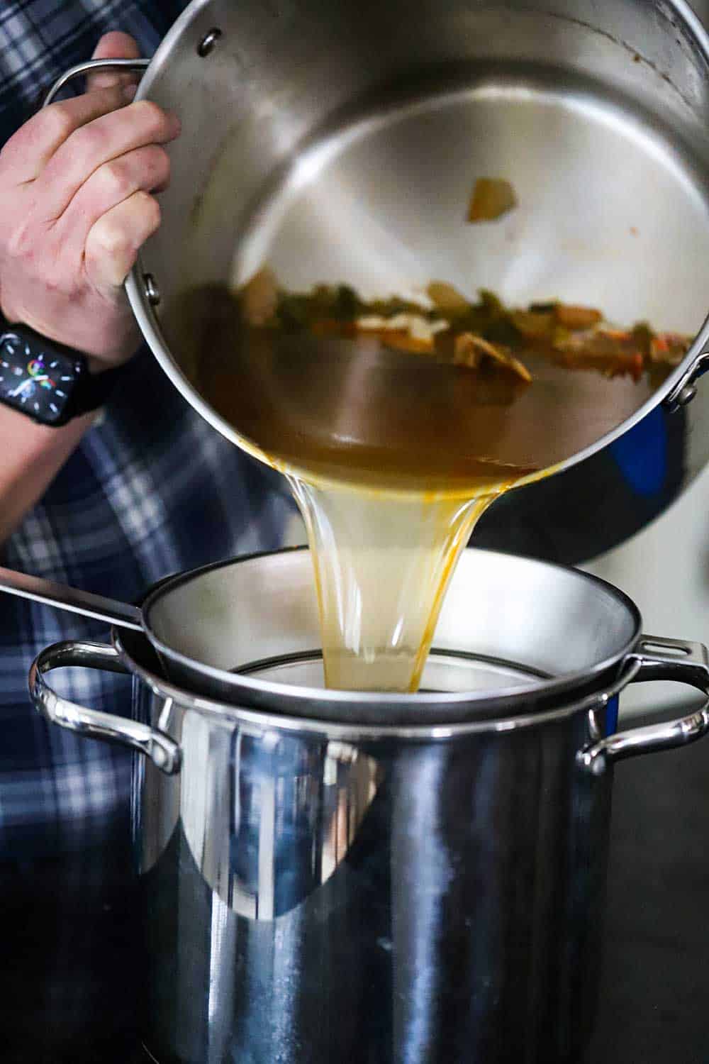 A person pouring shellfish stock and shrimp shells into a strainer sitting on a stock pot.