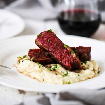 Two slices of Wagyu chuck short ribs that are stacked on top of mashed cauliflower all on a white dinner plate.