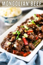 A white rectangular platter filled with prepared Mongolian beef and garnished with snipped chives and white sesame seeds.