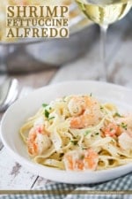 A white individual pasta bowl filled with shrimp fettuccine alfredo next to a large silver skillet filled with the same.