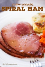 A white dinner plate filled with several slices of baked ham next to au gratin potatoes and braised carrots.
