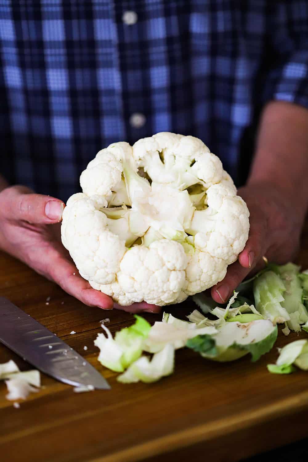 A person holding a head of cauliflower that has had the stems and some of the core removed.