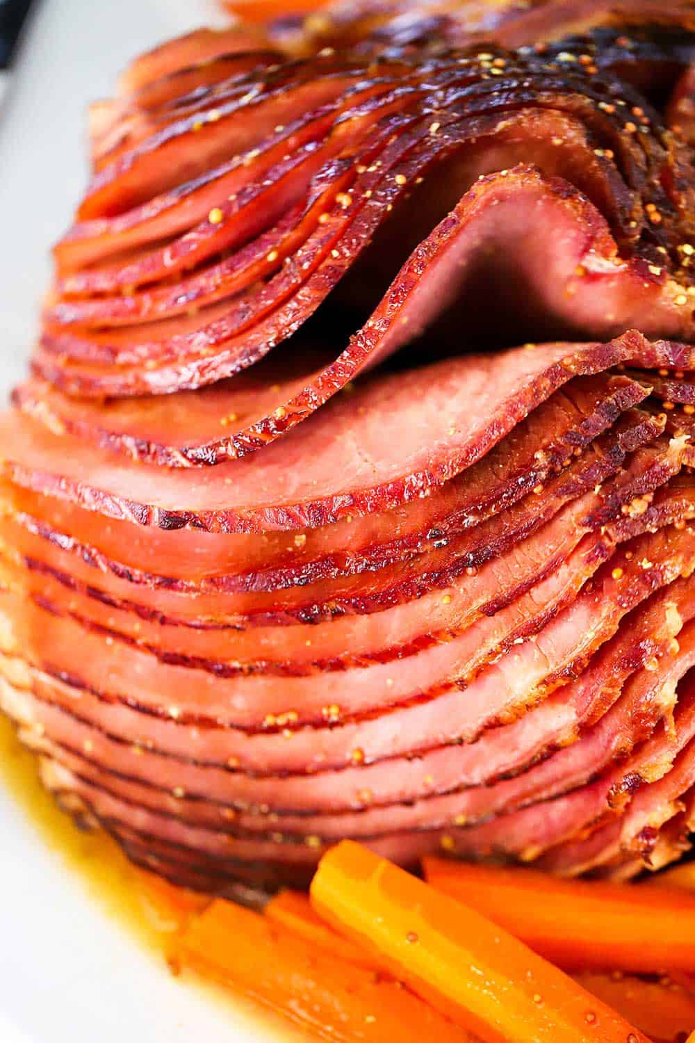 A fully cooked spiral ham that is on serving platter next to braised carrots. 