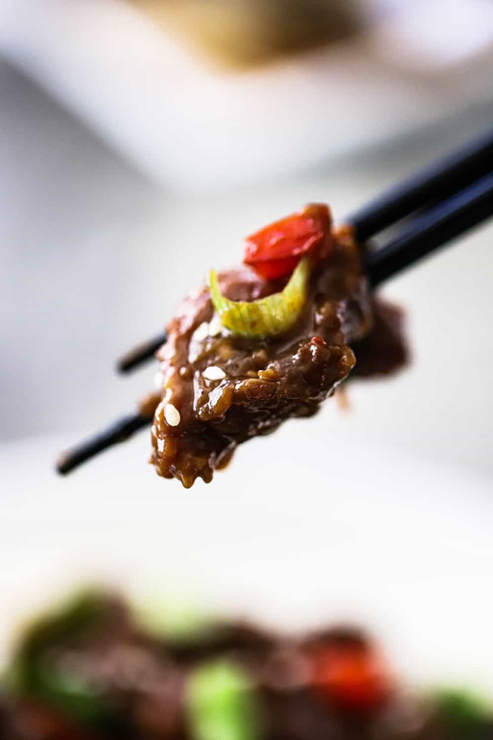 A pair of chop sticks holding up a piece of Mongolian beef. 