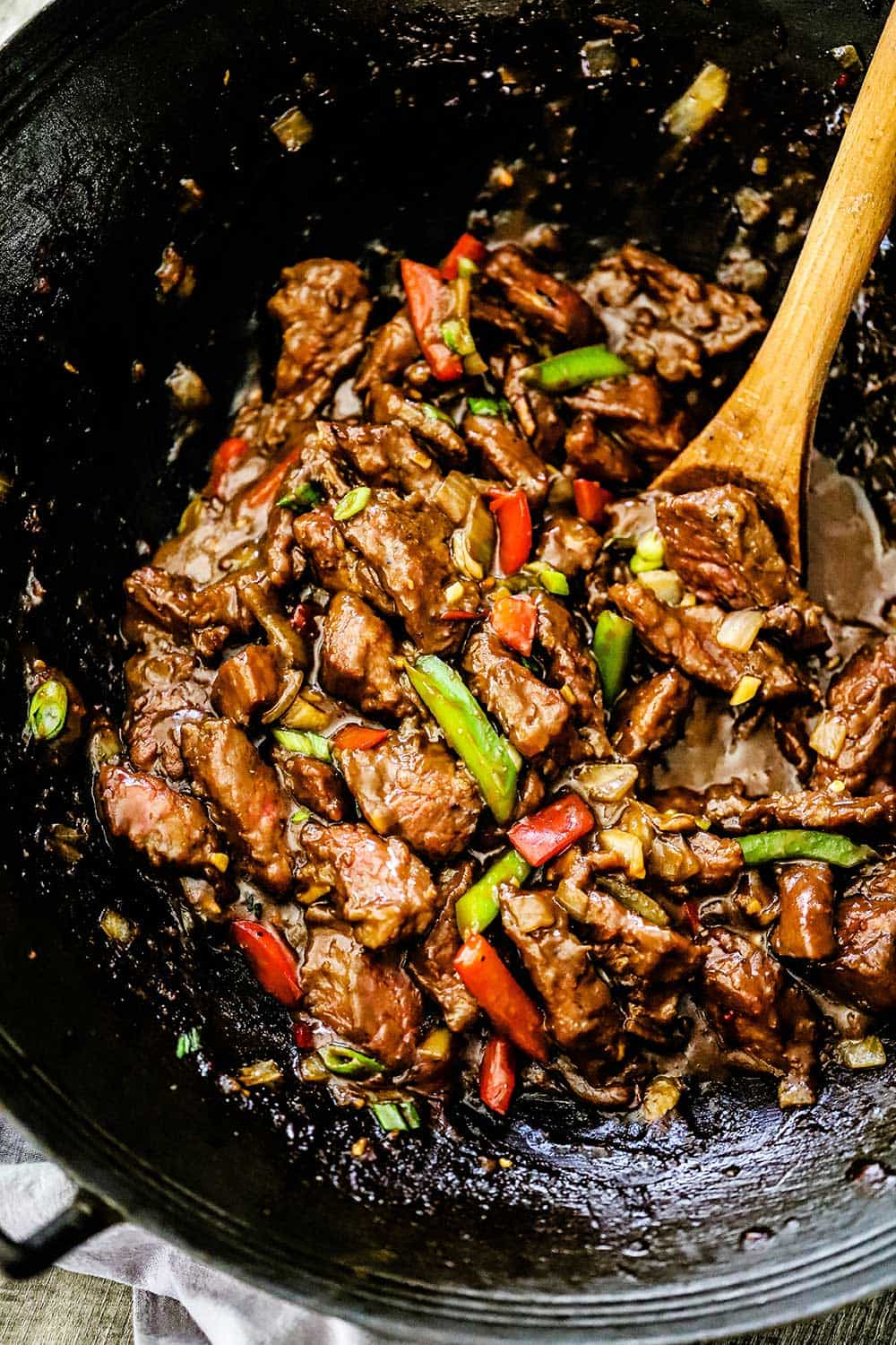 A wok filled with fully cooked mongolian beef with a wooden spoon inserted into the mixture. 