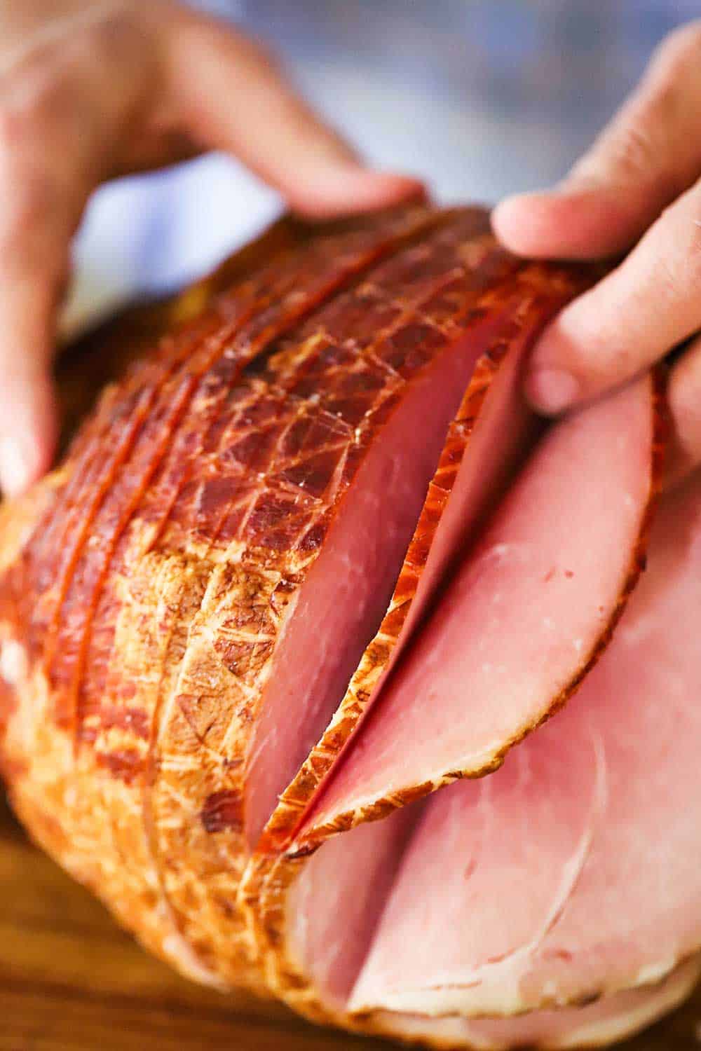 A pair of hands gently spreading apart a few of the slices of an spiral ham that is fully cooked. 