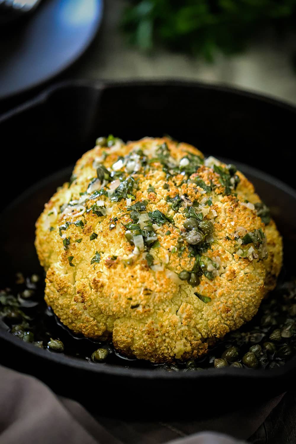 A whole roasted cauliflower with a wine butter herb sauce over the top all in a cast-iron skillet.