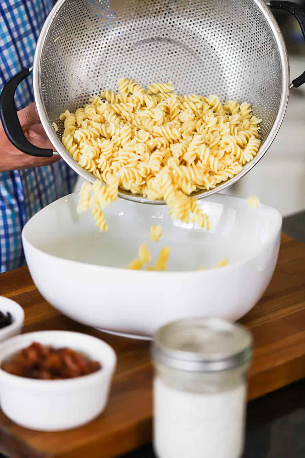 A person transferring cooked fusilli pasta from a colander into a white serving bowl. 