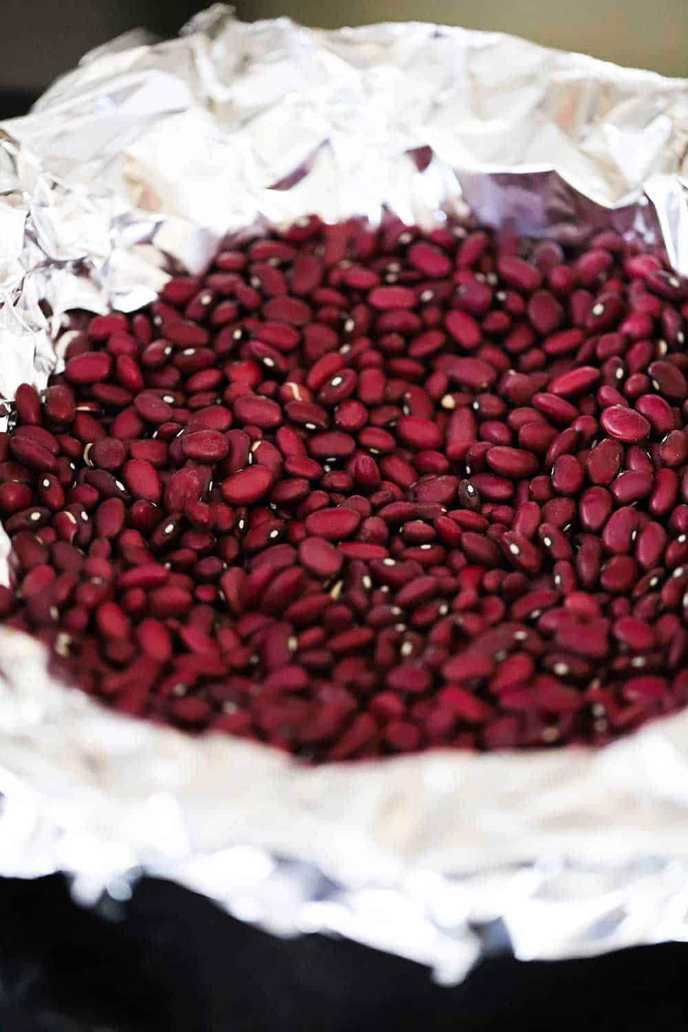 A pie dish that is lined with foil and then filled with dry red kidney beans.