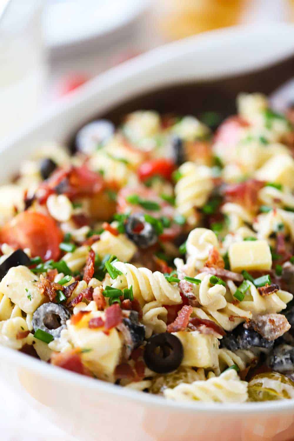 An oval white serving bowl filled with cheddar bacon Ranch pasta salad. 