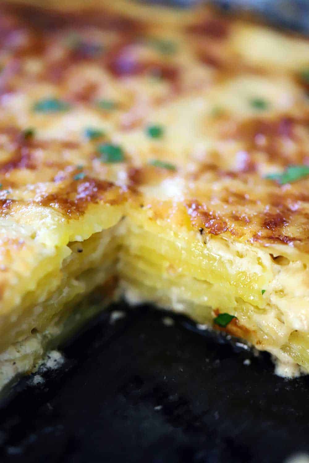 A dark baking dish filled with layers of potatoes dauphinoise with a square piece missing.