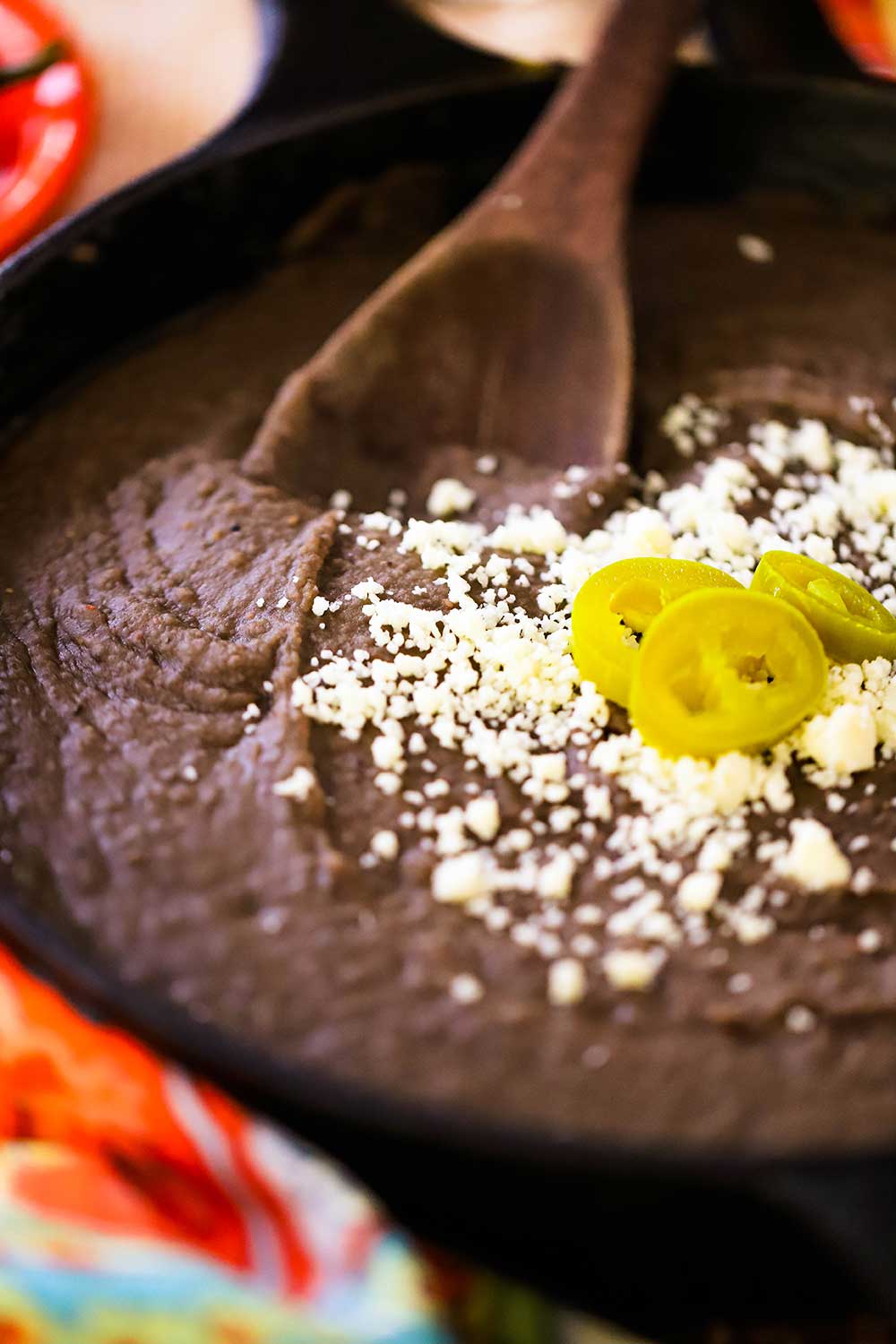 A cast-iron skillet filled with refried beans and topped with crumbled Cojita cheese and several jalapeno slices.