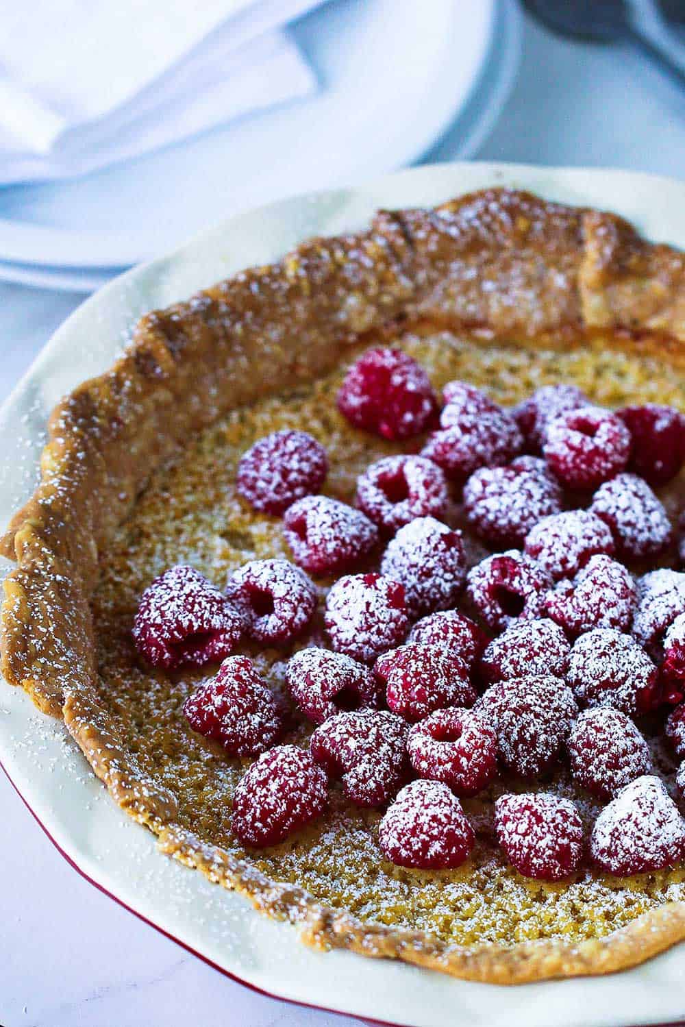 A whole chess pie topped with fresh raspberries and sprinkled with powdered sugar.