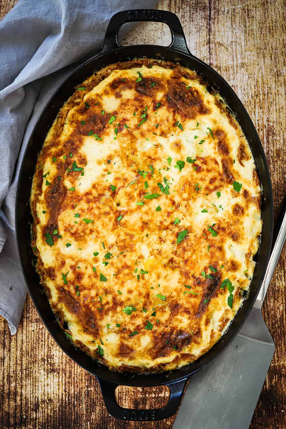 A large oval baking dish with handles filled with potatoes dauphinoise.