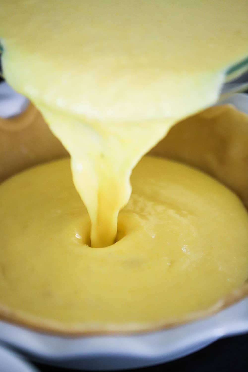 Yellow custard being poured into a pie dish filled with a baked pie crust.