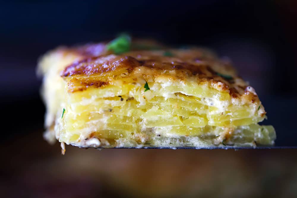 A slice of potatoes dauphinoise being raised up on a spatula.