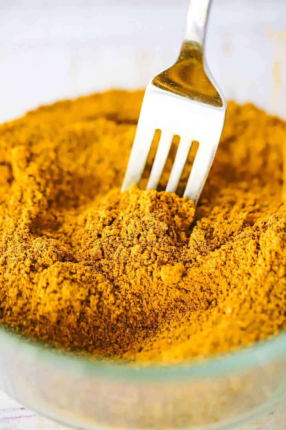 A glass bowl filled with Jamaican curry powder with a fork inserted into the middle of it. 