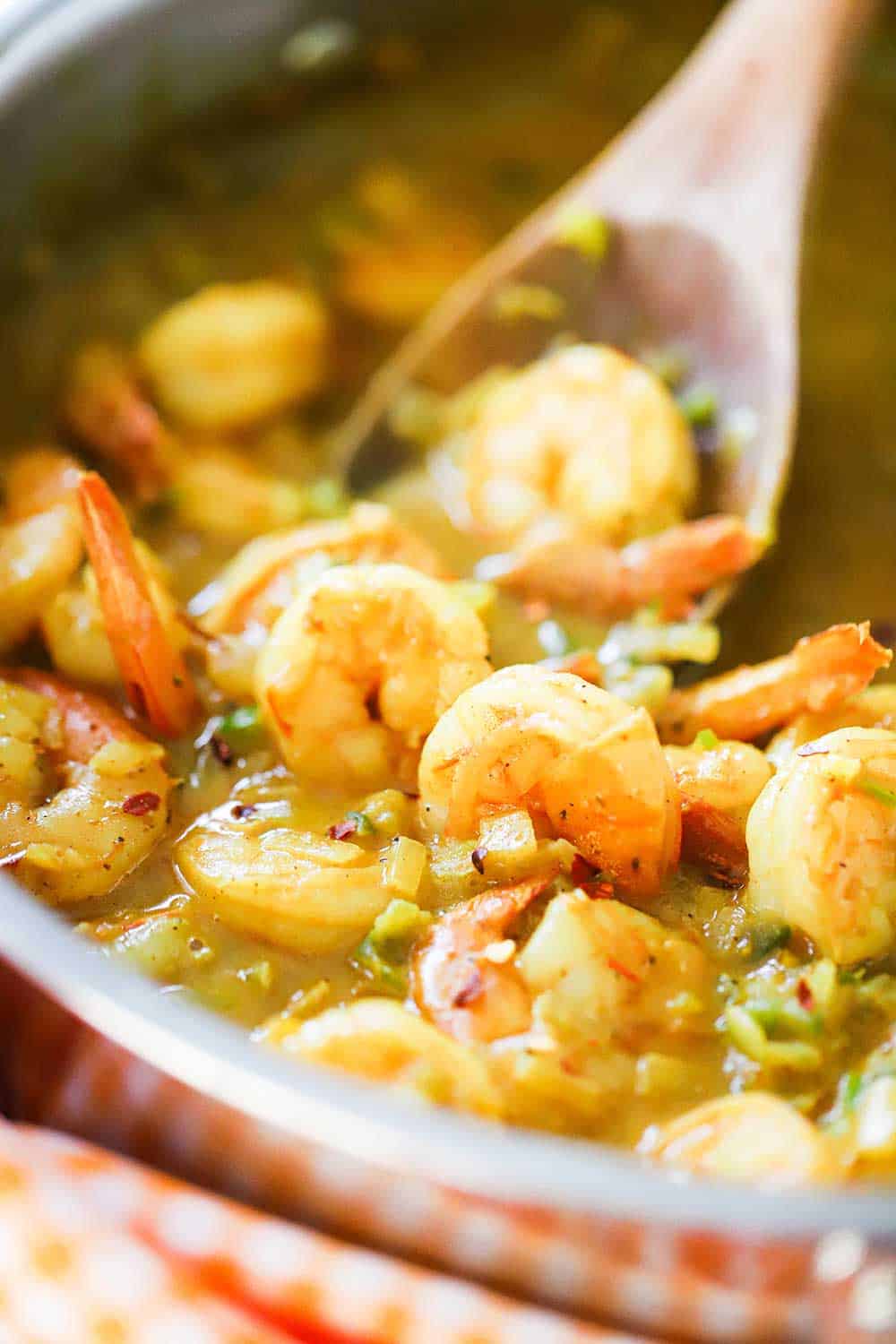 Shrimp curry being stirred in a large stainless steel skillet. 