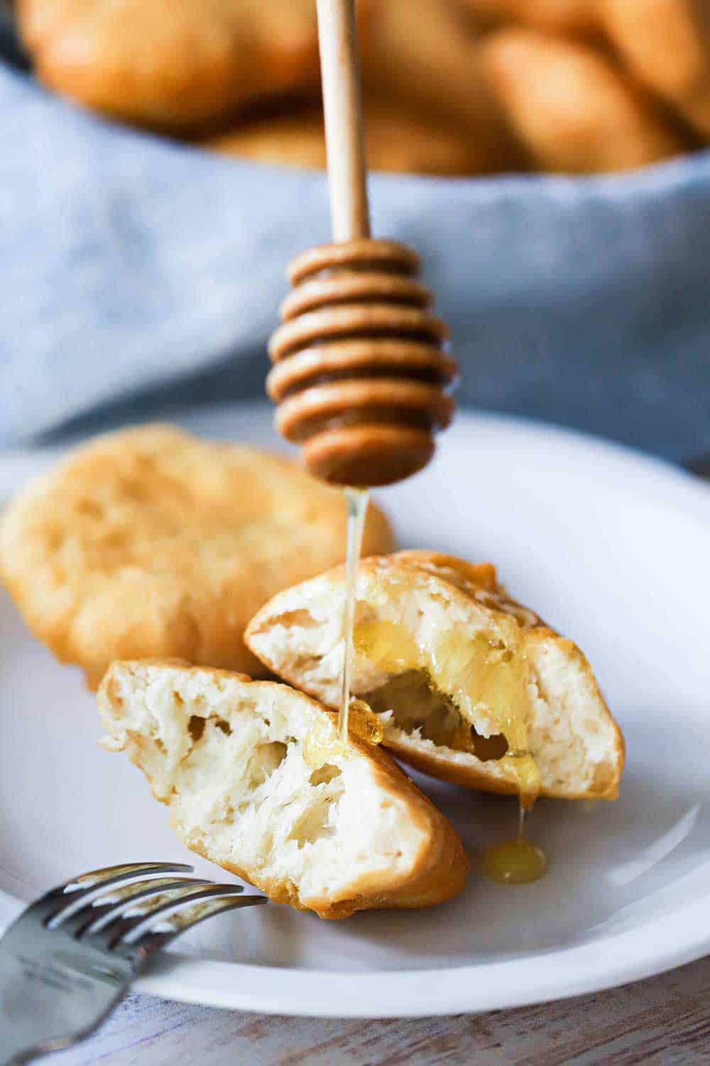 Honey being drizzled over a split-open Johnny cake on a white dessert cake. 