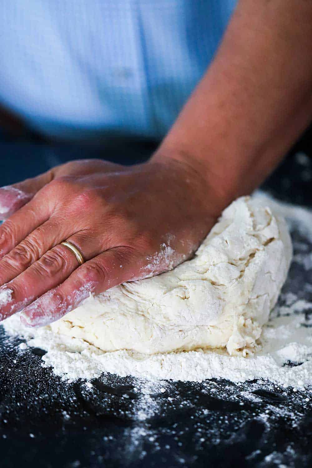 A person kneading dough on a floured black surface. 