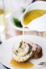 Two slices of an herb-stuffed pork loin roast on a dinner plate with white wine gravy being poured over them.