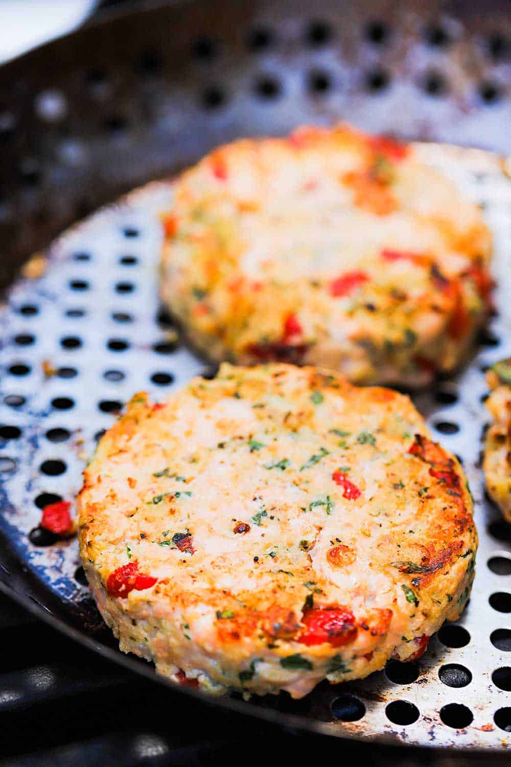 Two salmon burger patties being cooked on a grill pan on a gas grill. 