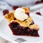 A single slice of cherry pie on a white dessert plate with a scoop of vanilla ice cream on top.