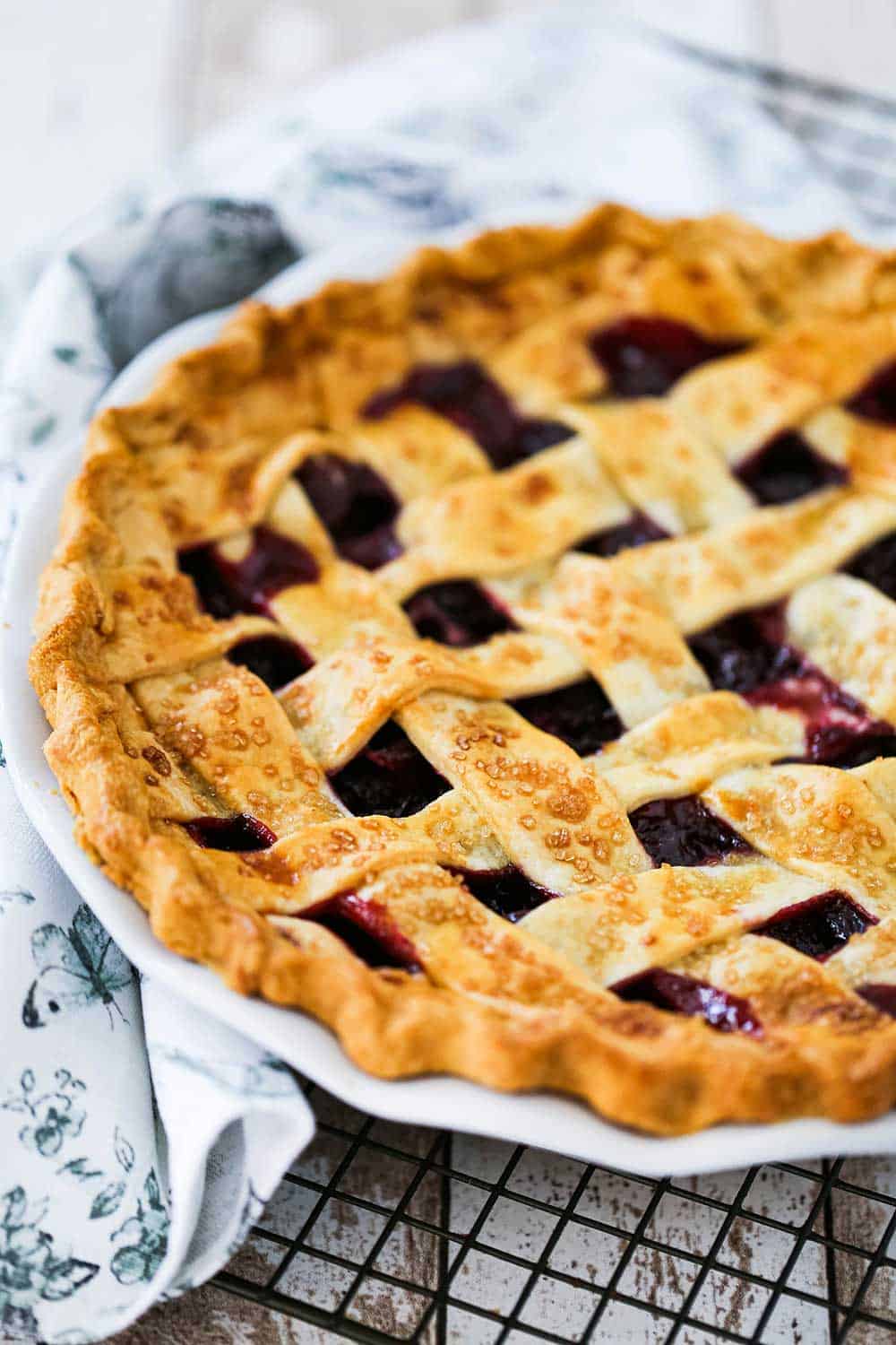 A white pie dish filled with a fully baked cherry pie with a lattice crust topping on it.