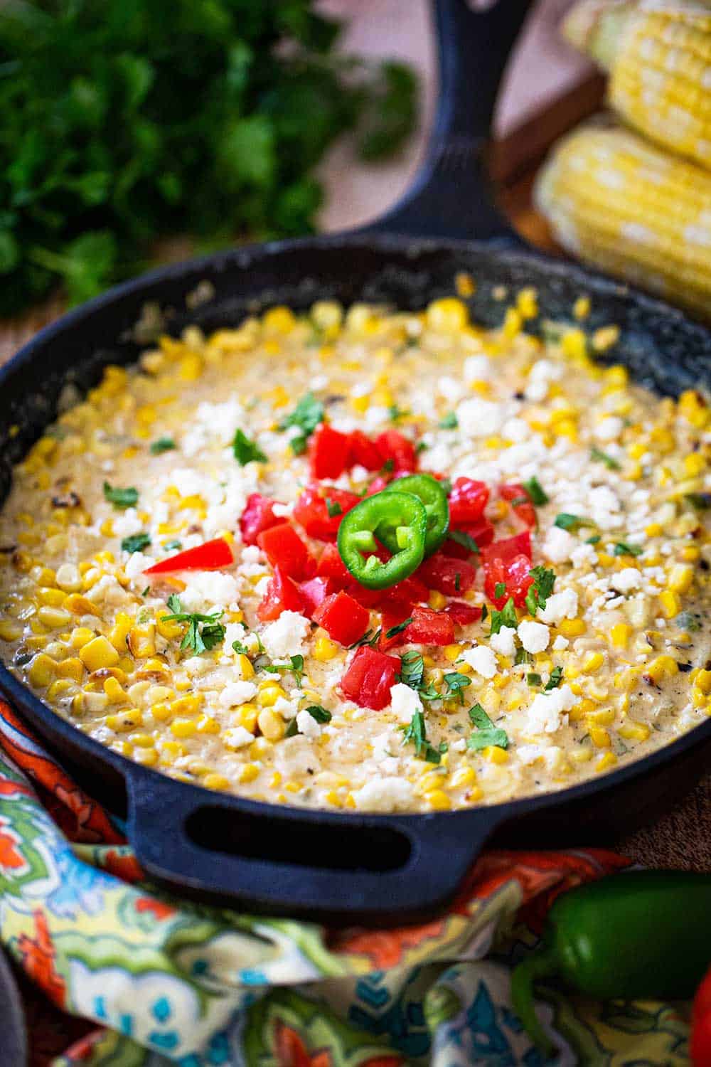 A cast-iron skillet filled with Mexican cream corn topped with crumbled queso fresco, chopped tomatoes, and chopped cilantro.