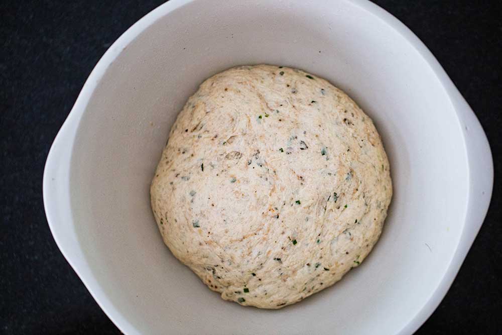 A white ceramic bowl filled with grissini dough that has risen overnight. 