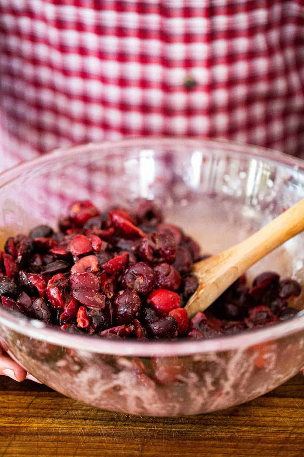 A person in a red checkered shirt standing behind a bowl filled with cherry pie filling.