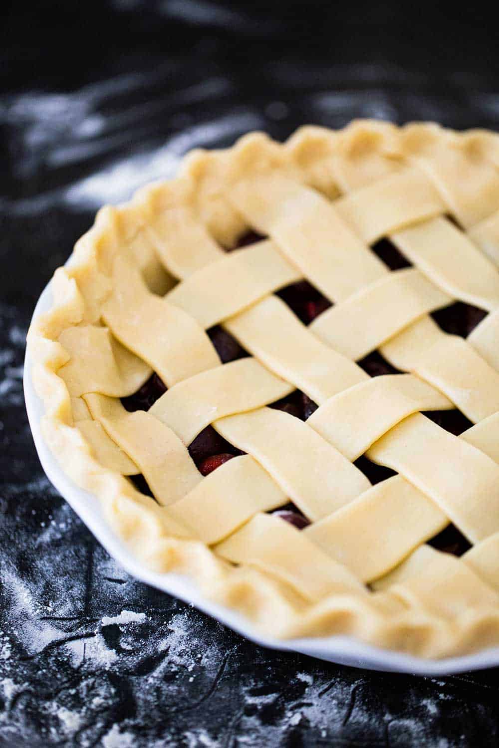 An unbaked cherry pie in a white pie dish with strips of pie dough on top in a lattice formation.