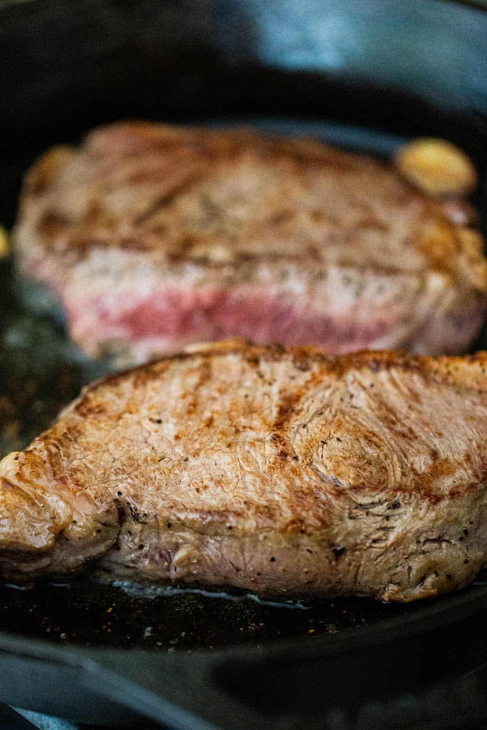 Two seared ribeye steaks simmering in a cast-iron skillet.