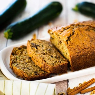 A loaf of freshly baked zucchini bread that has a couple of slices cut on an small platter.
