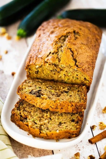 A loaf of freshly baked zucchini bread that has a couple of slices cut on an small platter.