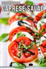 A platter of caprese salad that has been drizzled with pesto sauce and a balsamic glaze and topped with freshly chopped basil.