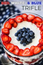 The top of a red, white, and blue trifle that is garnish with an outer circle of fresh, sliced strawberries, and then a pile of fresh blueberries in the center, all sitting on white cream sauce.